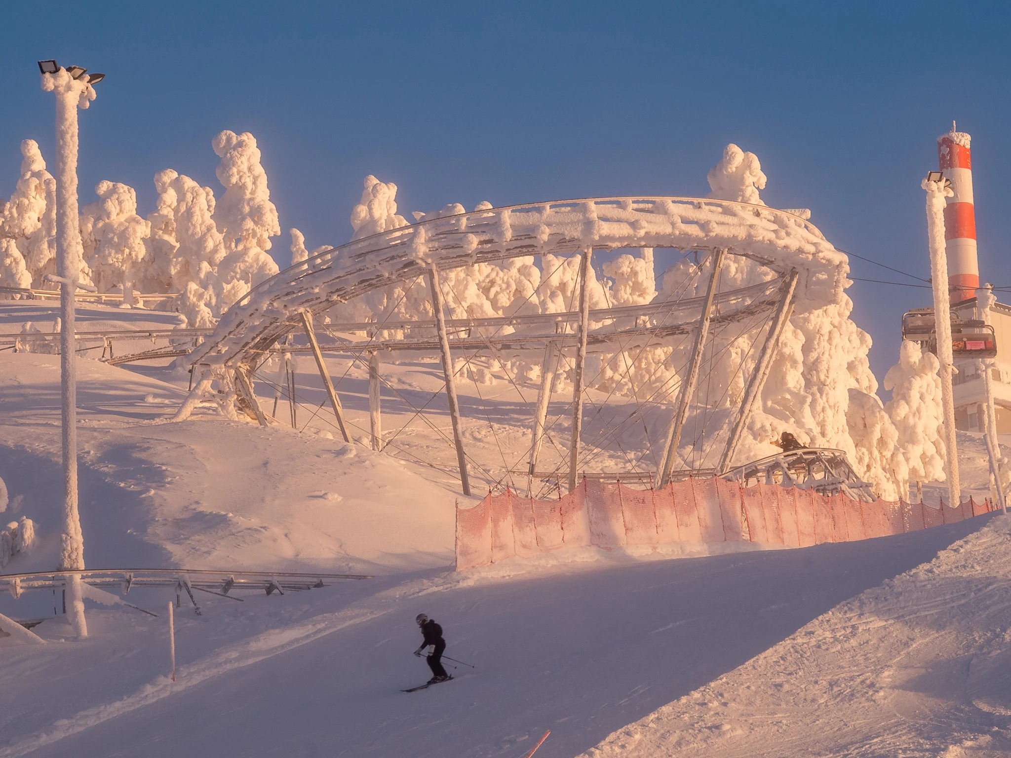 Ruka Coaster vuoristorata tekee silmukan lumisessa maisemassa iltaauringon loisteessa