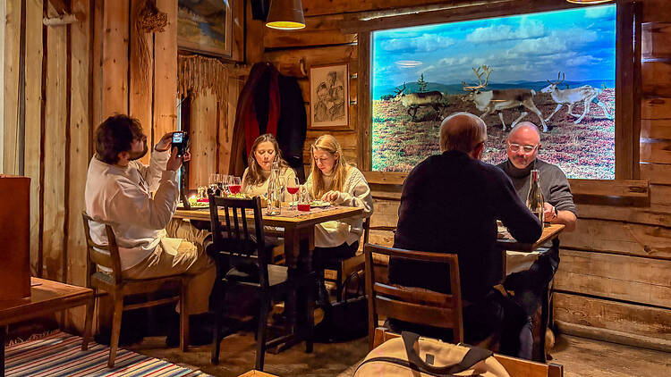 Ihmisiä istumassa pöydissä Lappi ravintolassa jossa on puiset lautaseinät
