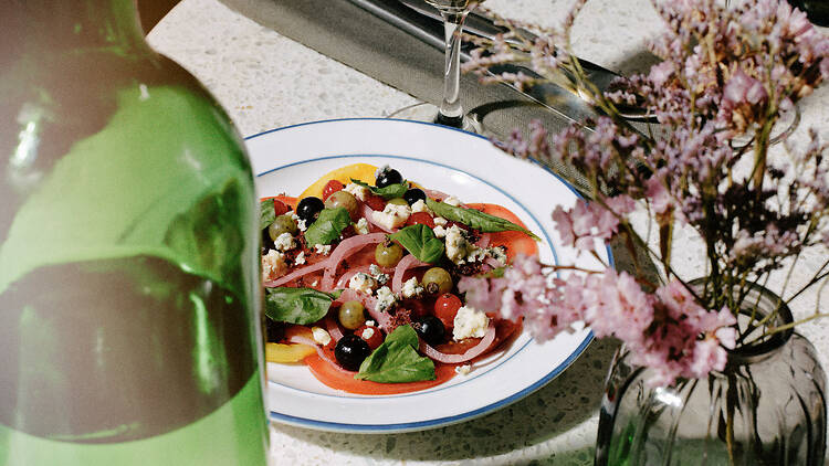 lautasellinen tomaattisalaattia näkyy vesipullon ja kuivakukkien välistä ravintolassa Nolita