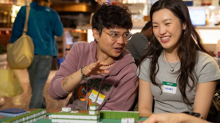 The New York Games Two people talking over mahjong tiles