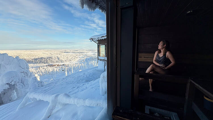 A woman sits in a sauna, a large window framing a snow-covered landscape beyond. A woman sits in a sauna, a large window framing a snow-covered landscape beyond.