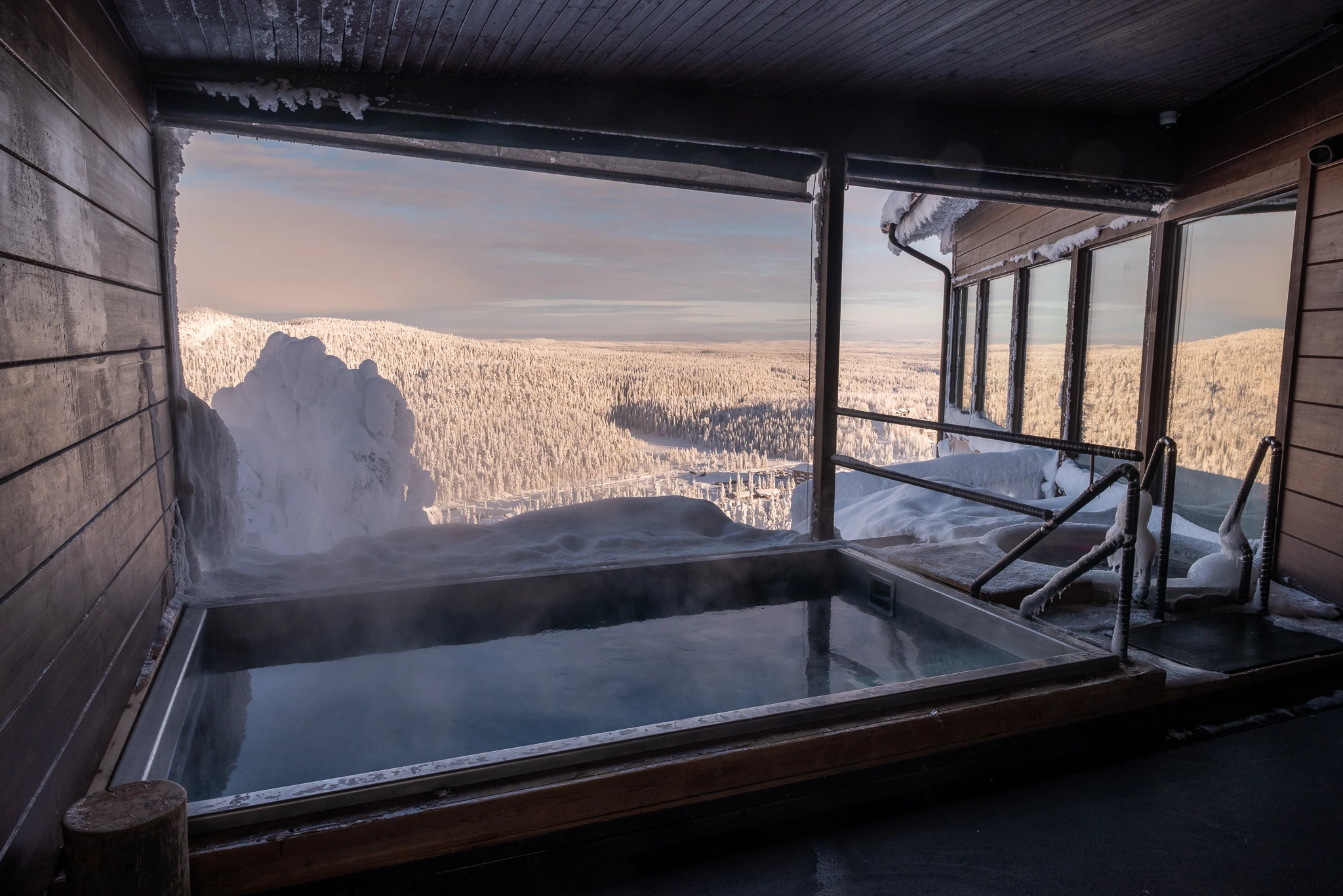 Steam rises from the warm outdoor pool, with snow-covered landscapes stretching out beyond.