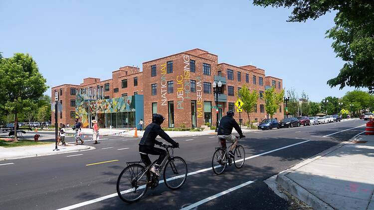 Cyclists bike past the exterior of the National Public Housing Museum.