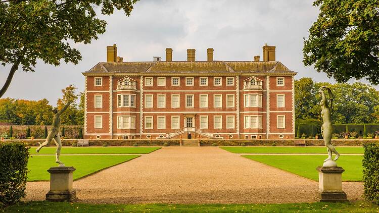 Exterior shot of Ham House from the end of pathway leading up to it, framed by two statues