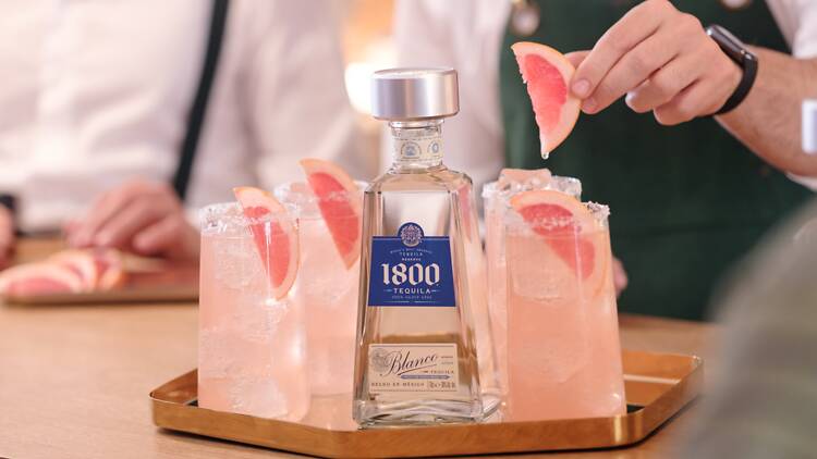 A serving of four Paloma cocktails on a tray with 1800 Tequila bottle