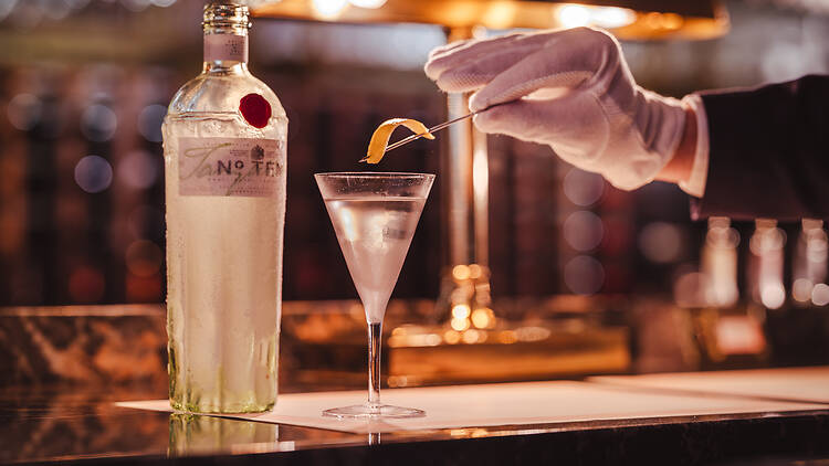 White-gloved hand garnishing gin martini with a twist