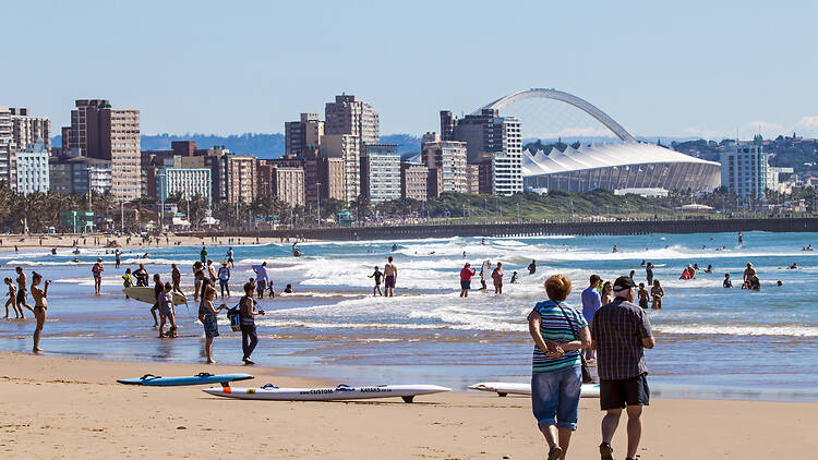 Many unknown people on morning visit to beach against Durban city skyline and Moses Mabhida Stadium  in South Africa