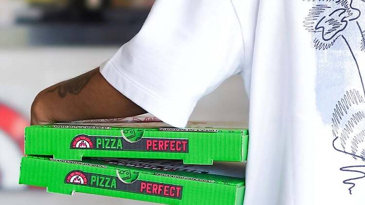 A person in white shirt holding Pizza Perfect boxes