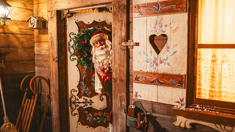 Santa poking his head round the door of a festive cottage