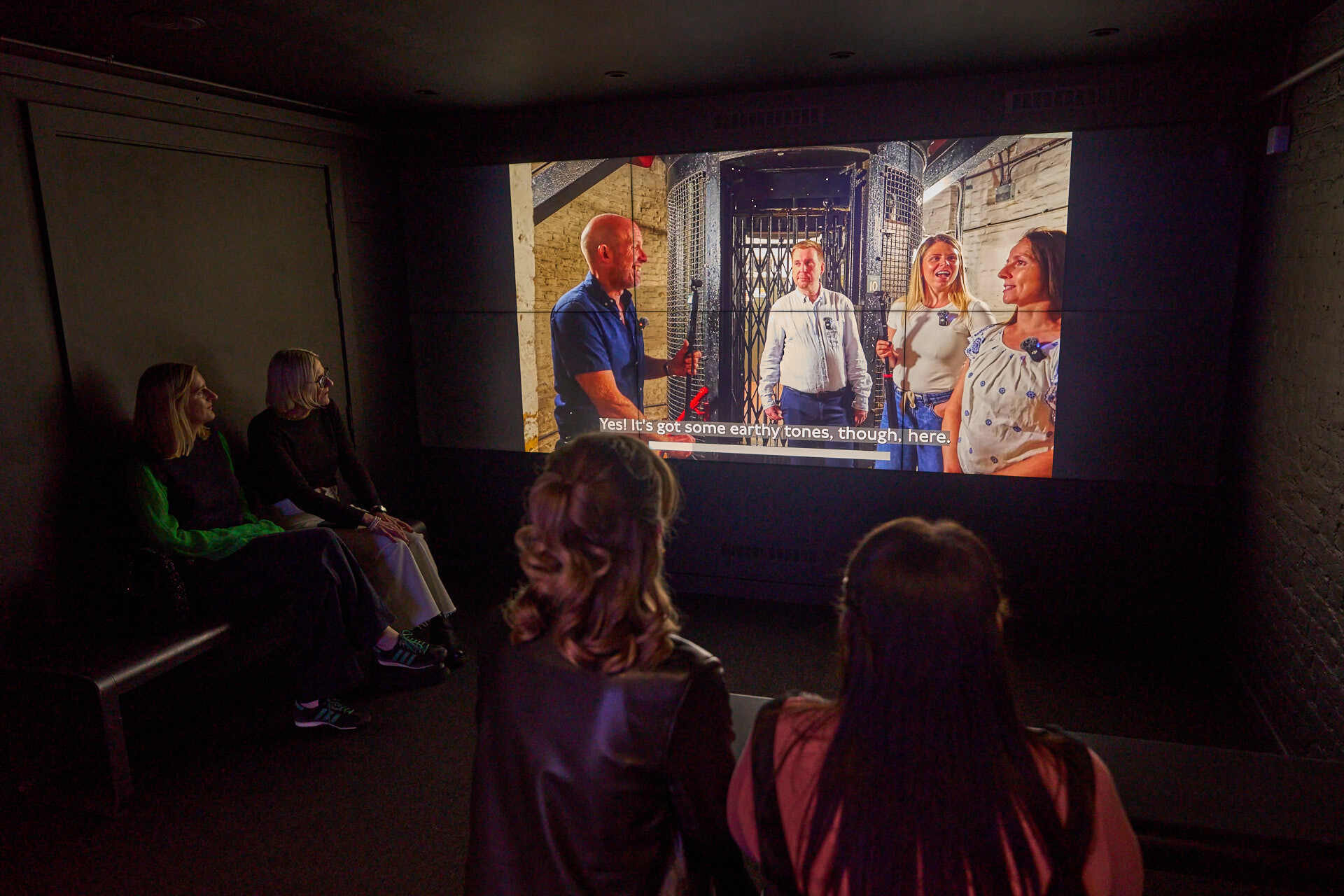 Four people watch a video on London transport in dark room
