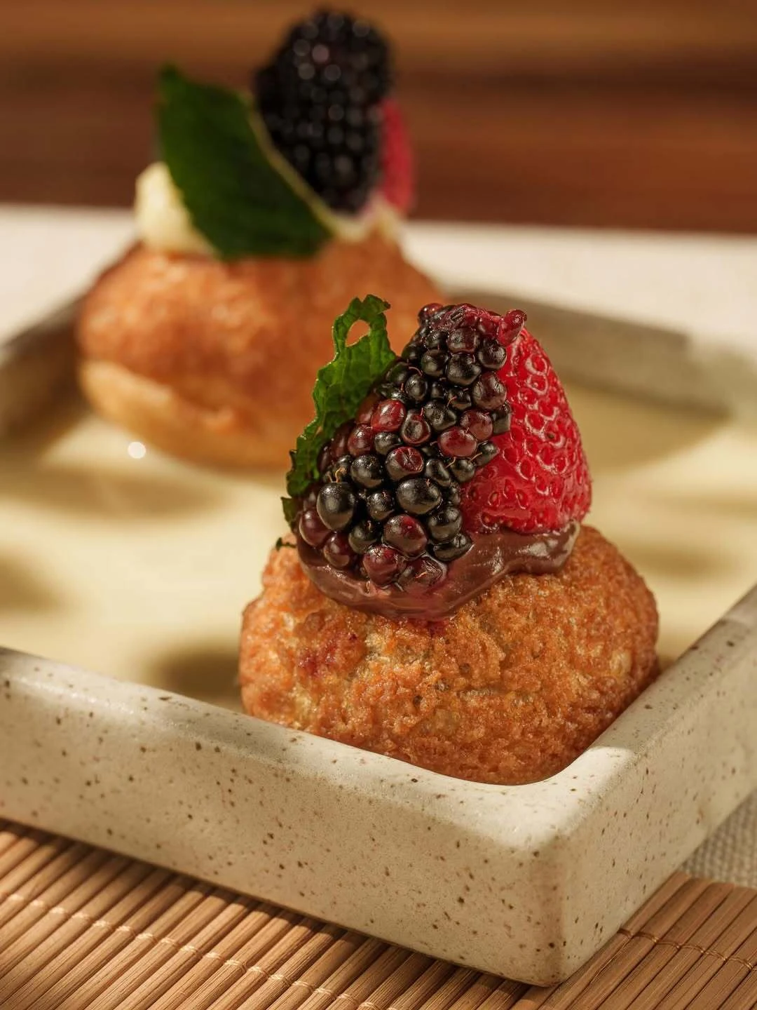 Duo de Choux com ganache de cupua&ccedil;u e chocolate branco e ganache de chocolate meio amargo, servido com creme ingl&ecirc;s com puxuri, finalizada com frutas vermelhas