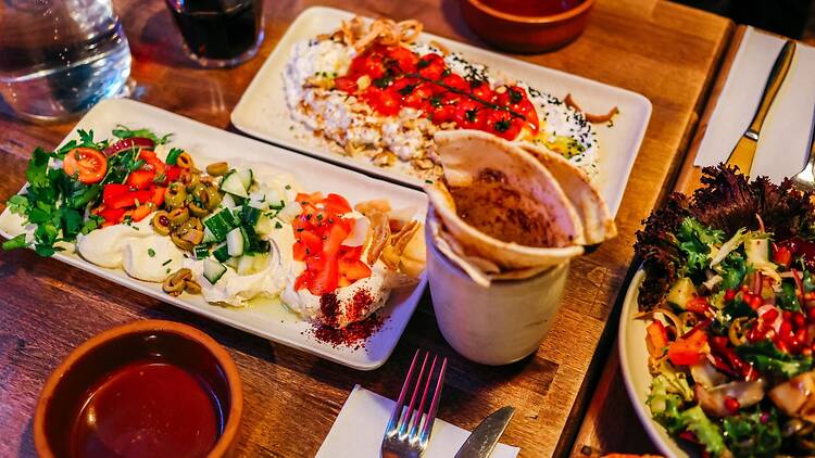 Pöydällä on lautasia täynnä värikkäitä välimerellisiä mezejä, tuoreita kasviksia ja lämpimiä pita-leipiä.