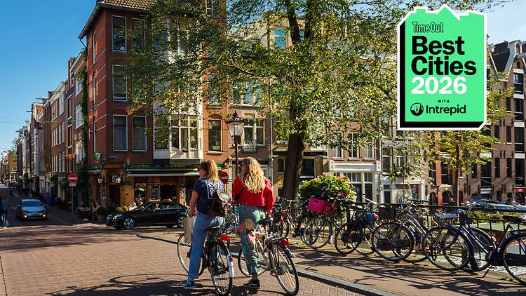 Two people cycling in Amsterdam on a sunny day. A badge in the right-hand corner of the image reads 'Best Cities 2026 with Intrepid'.