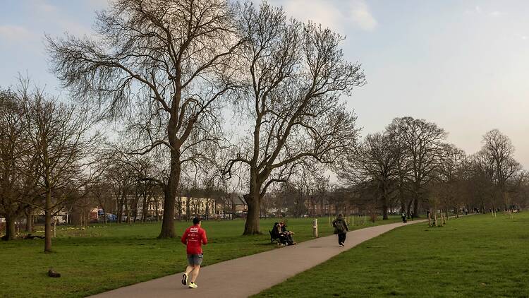 A man wearing shorts and a red jacket running down a path in Brockwell Park