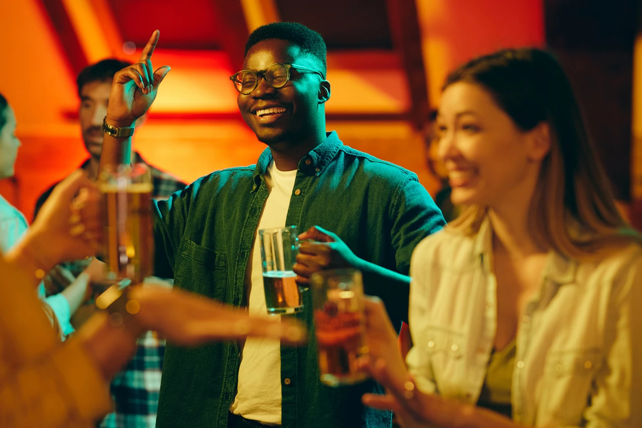 Young happy Black man drinking beer and enjoying with his friends in a pub at night.