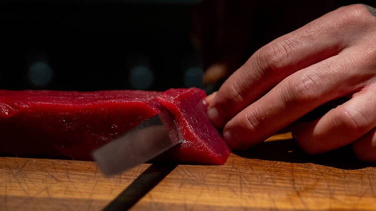 kokki leikkaa veitsellä tonnikalan punaisesta lihasta palasta ravintolassa Shii Helsingissä