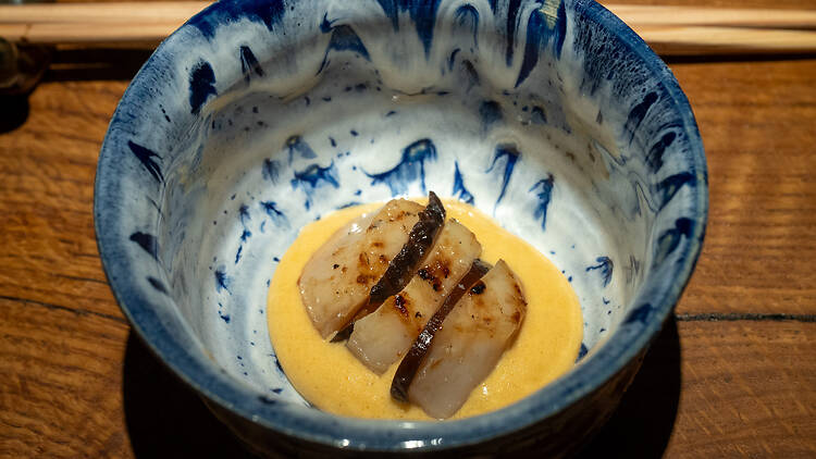 Syvällä lautasella keltaista kastiketta ja grillatun kampasimpukan sekä sienen palasia ravintolassa Shii