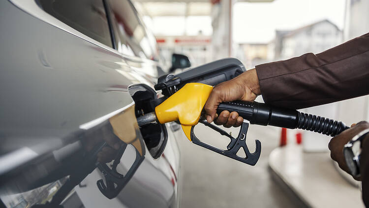 Close up of interracial man's hand holding nozzle and pouring gasoline at gas station.