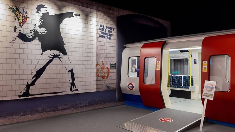 Kuva näyttelystä jossa Banksyn maalaus esittää mielenosoittajaa heittämässä polttopullon sijaan kukkakimppua vierellään metrovaunu