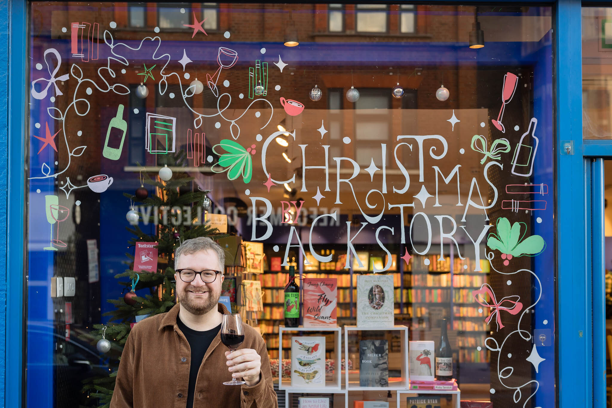 Owner Tom Rowley holds glass of wine in front of his bookshop window display