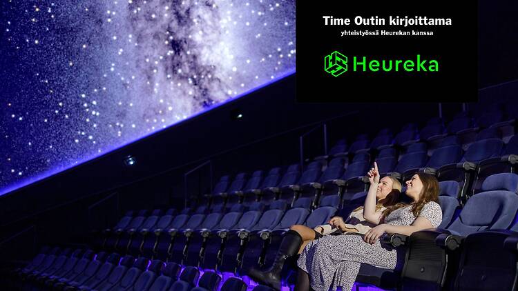 Kaksi naista istuu katsomossa ja katselee planetaarion näyttöä tyytyväisenä. 