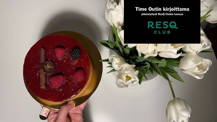 Henkilö pitää kädessään punaista marjakakkua valkoisten tulppaanien vieressä pyöreällä pöydällä.