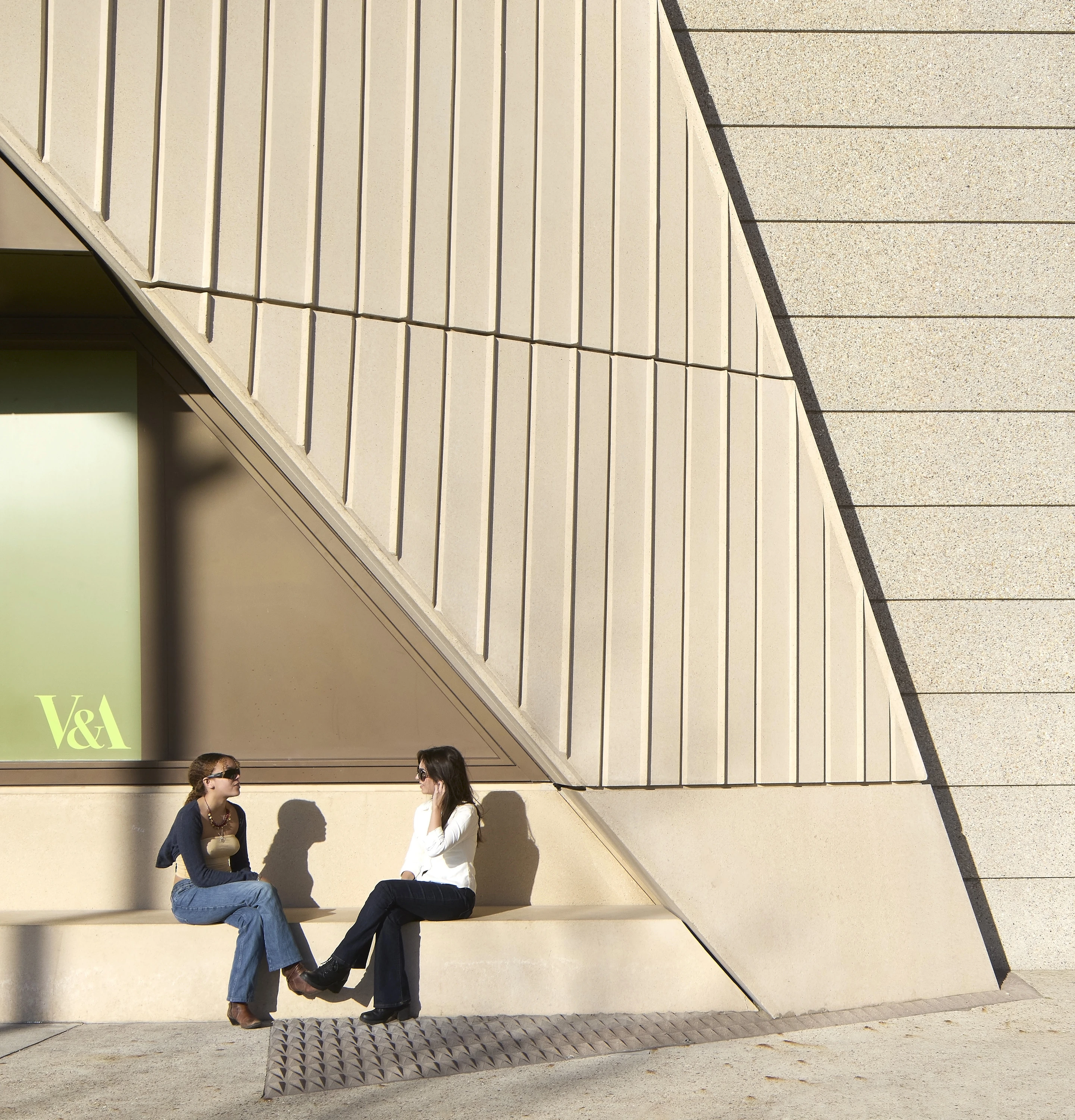 Two women sit chatting on built-in bench outside new museum