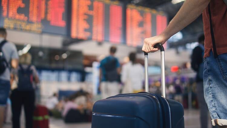 A man's hand holding a suitcase handle in an airport