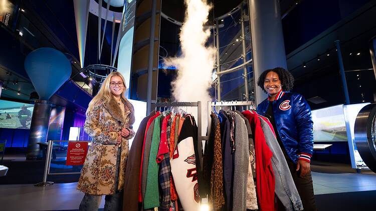 Shoppers at Thrift Lab pose with a garment rack in front of the 'Science Storms' exhibit.