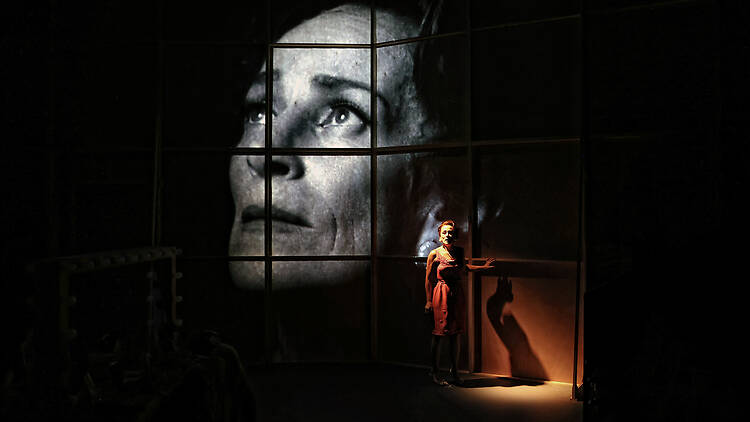 A woman's face on a screen in black and white, and a woman standing on stage in front of it