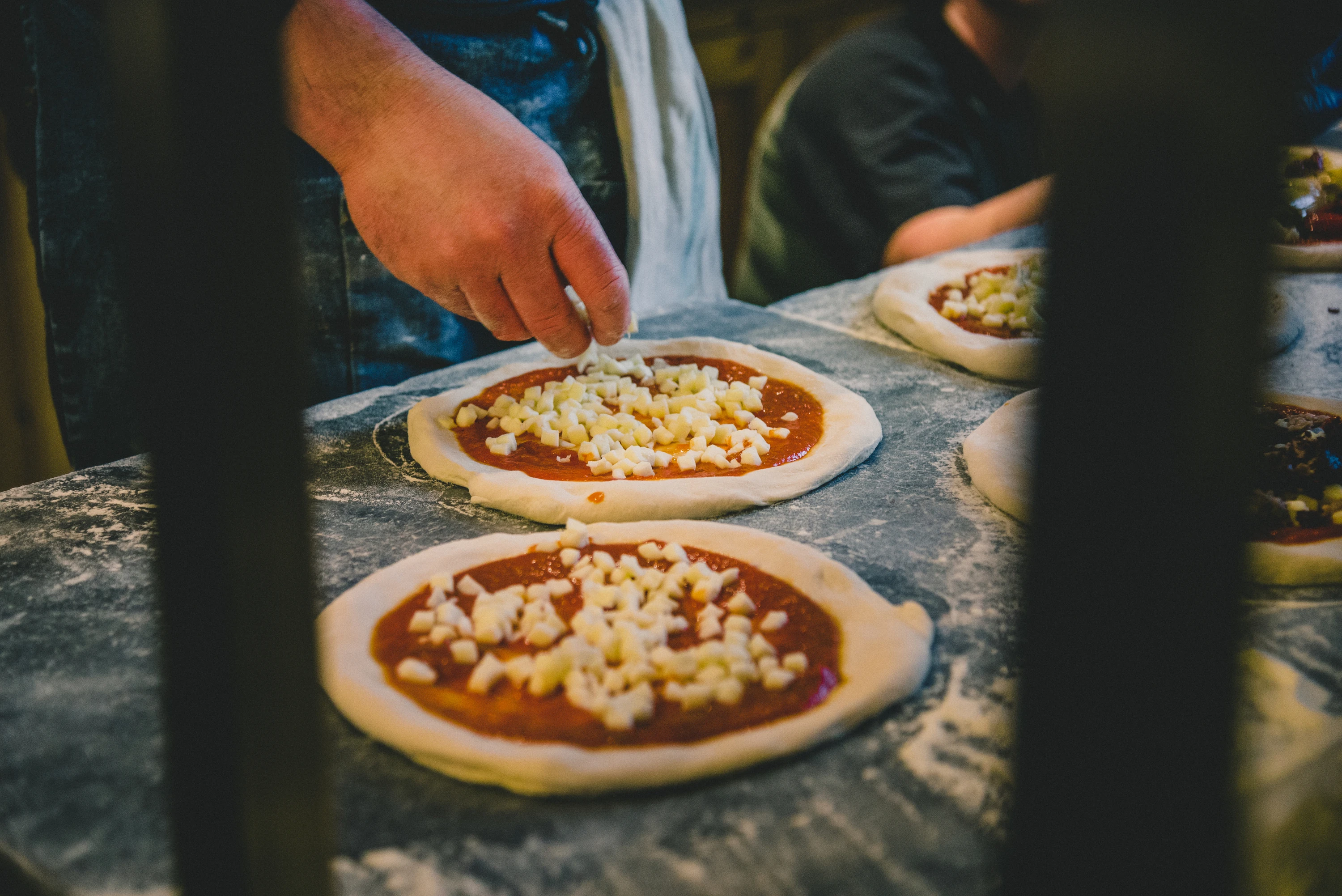 Chef adding cheese to raw pizza dough with tomato sauce