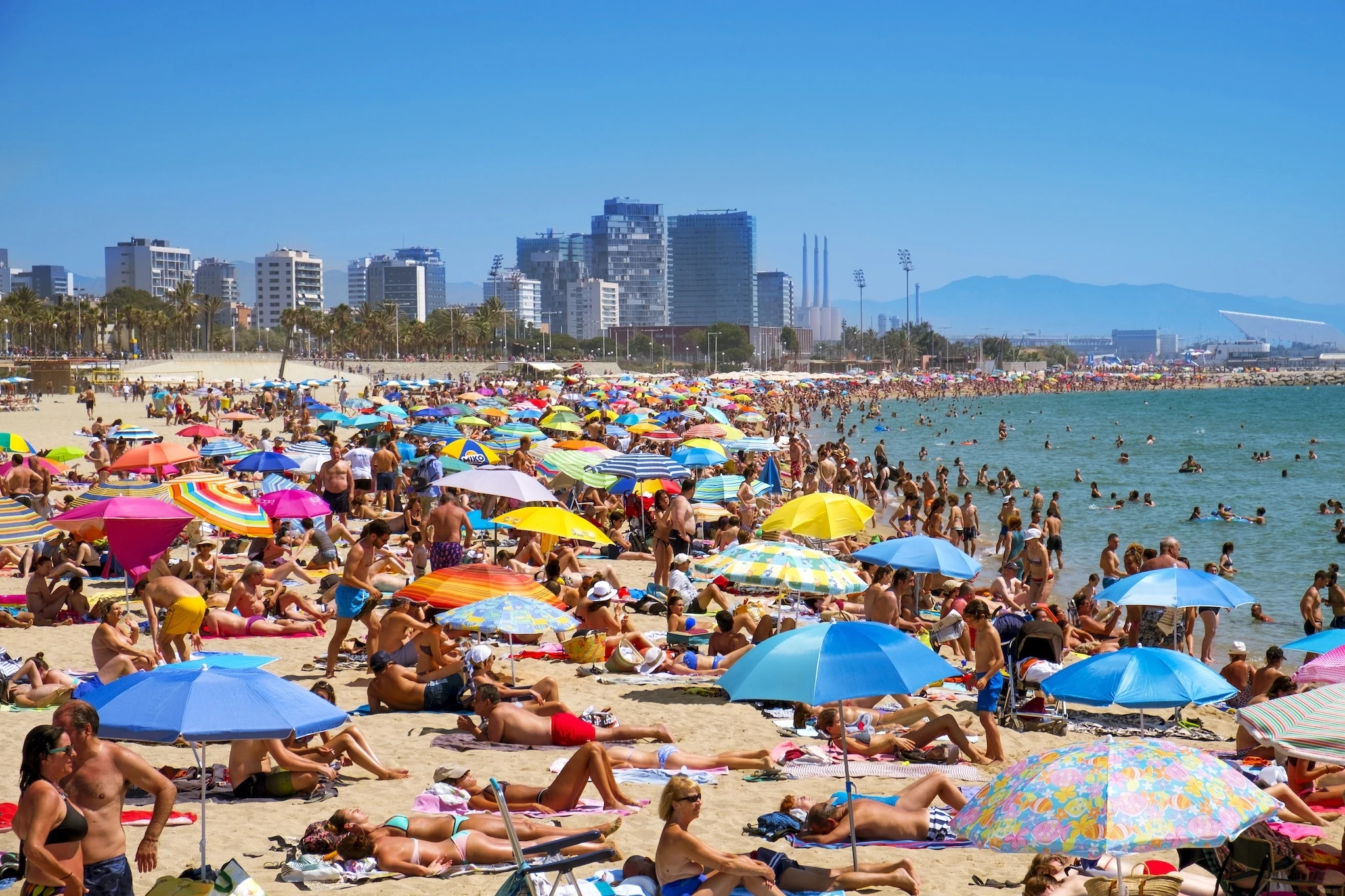 Sunbathers at Platja del Bogatell beach in Barcelona, Spain, with the Parc del Forum in the background