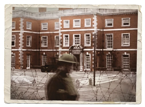 A historical photo of a WWII soldier standing outside Trent Park House, with barbed wire surrounding the house