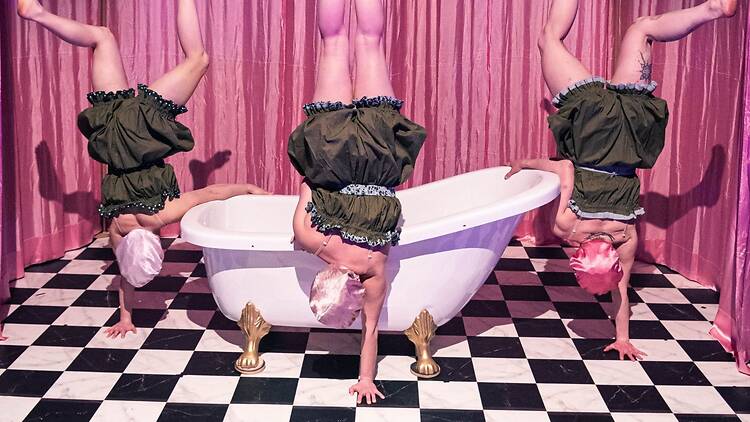 Kolme sirkustaiteilijaa seisoo yhdellä kädellä kylpyammeen ympärillä