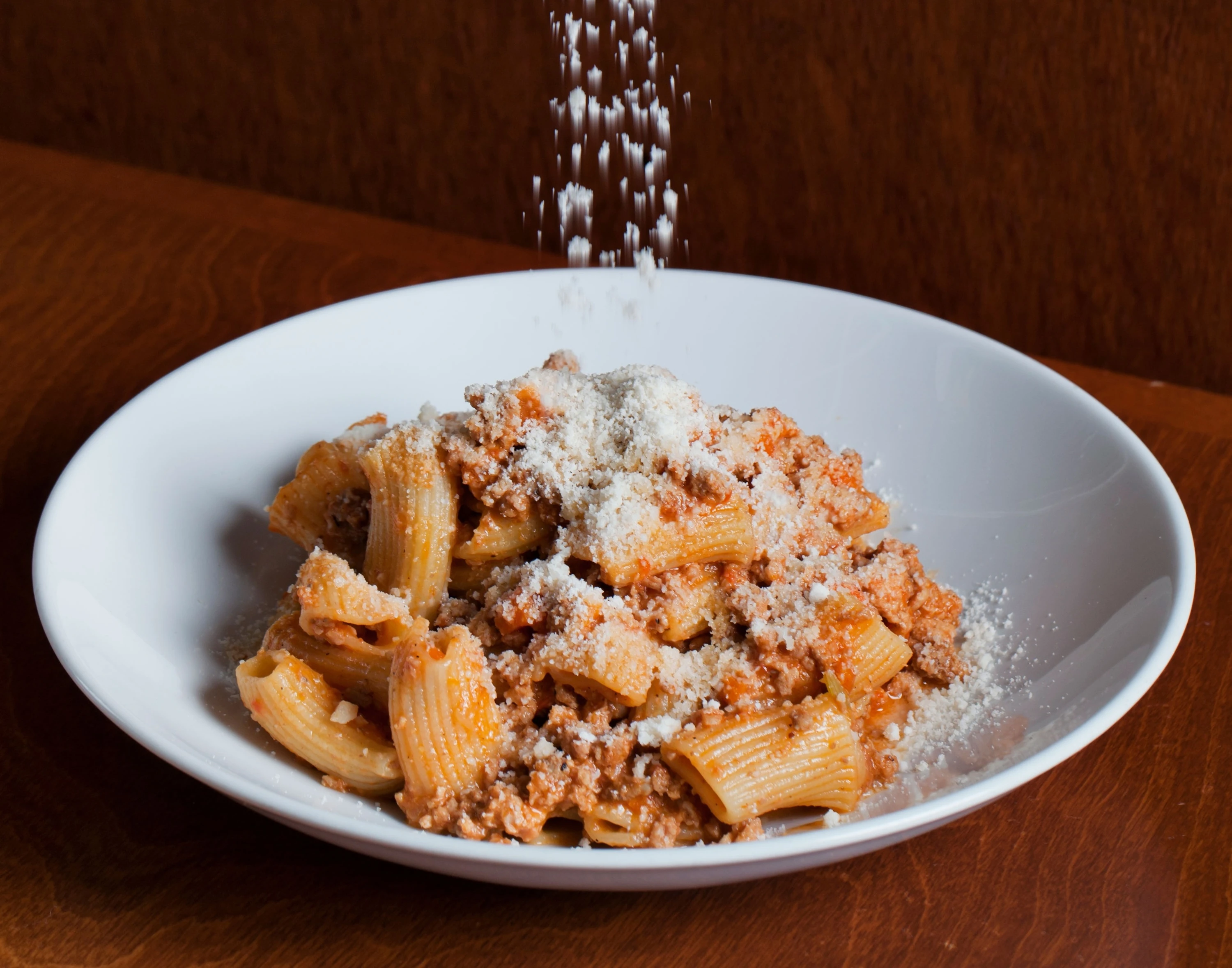 A plate of pasta being sprinkled by parmesan