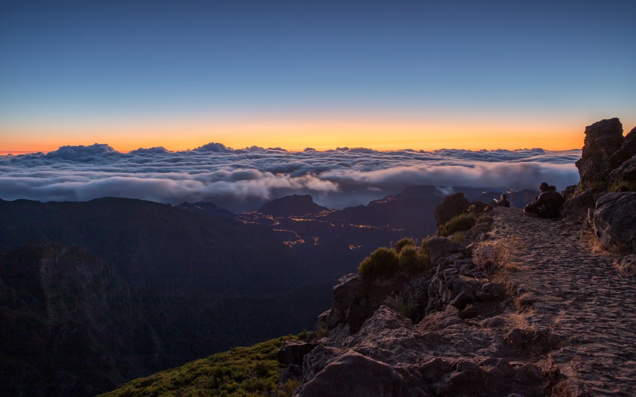 The lights from Machico twinkle as the sun rises over the clouds above Madeira seen from Pico do Areeiro.