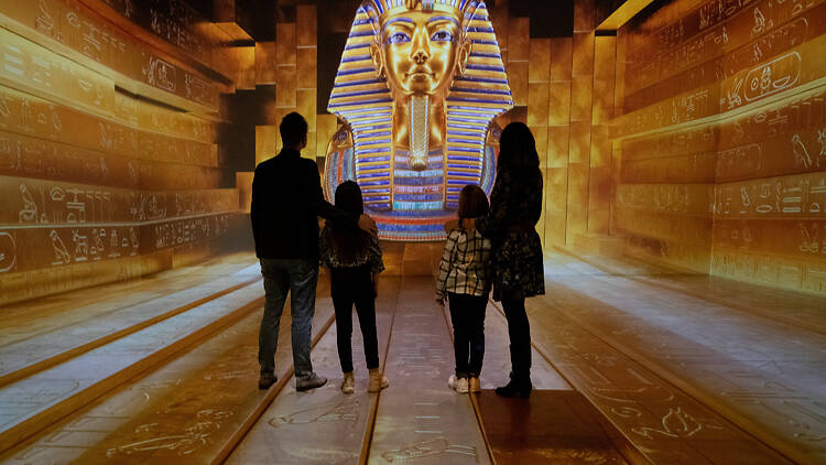 A family immersed in Tutankhamun: The Immersive Exhibition with pharaoh head on screen 