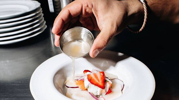 A hand pouring a sauce over strawberries