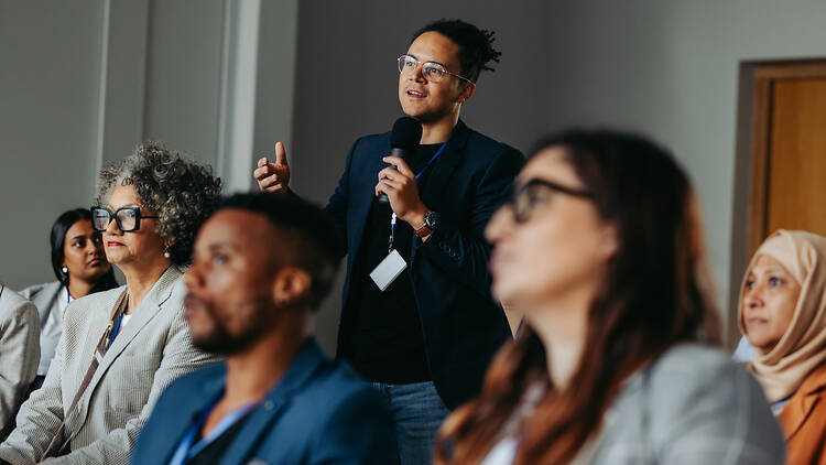 2197783537 Businessman asking a question during a diverse conference workshop presentation. Attendees are engaged and listening attentively.