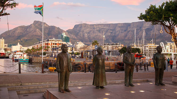 The Nobel Square sculptures of  Albert Lutuli, Desmond Tutu, F. W. de Klerk, and Nelson Mandela at Victoria and Albert waterfront pier, and the table mountain in the back at sunset, Cape Town, South Africa