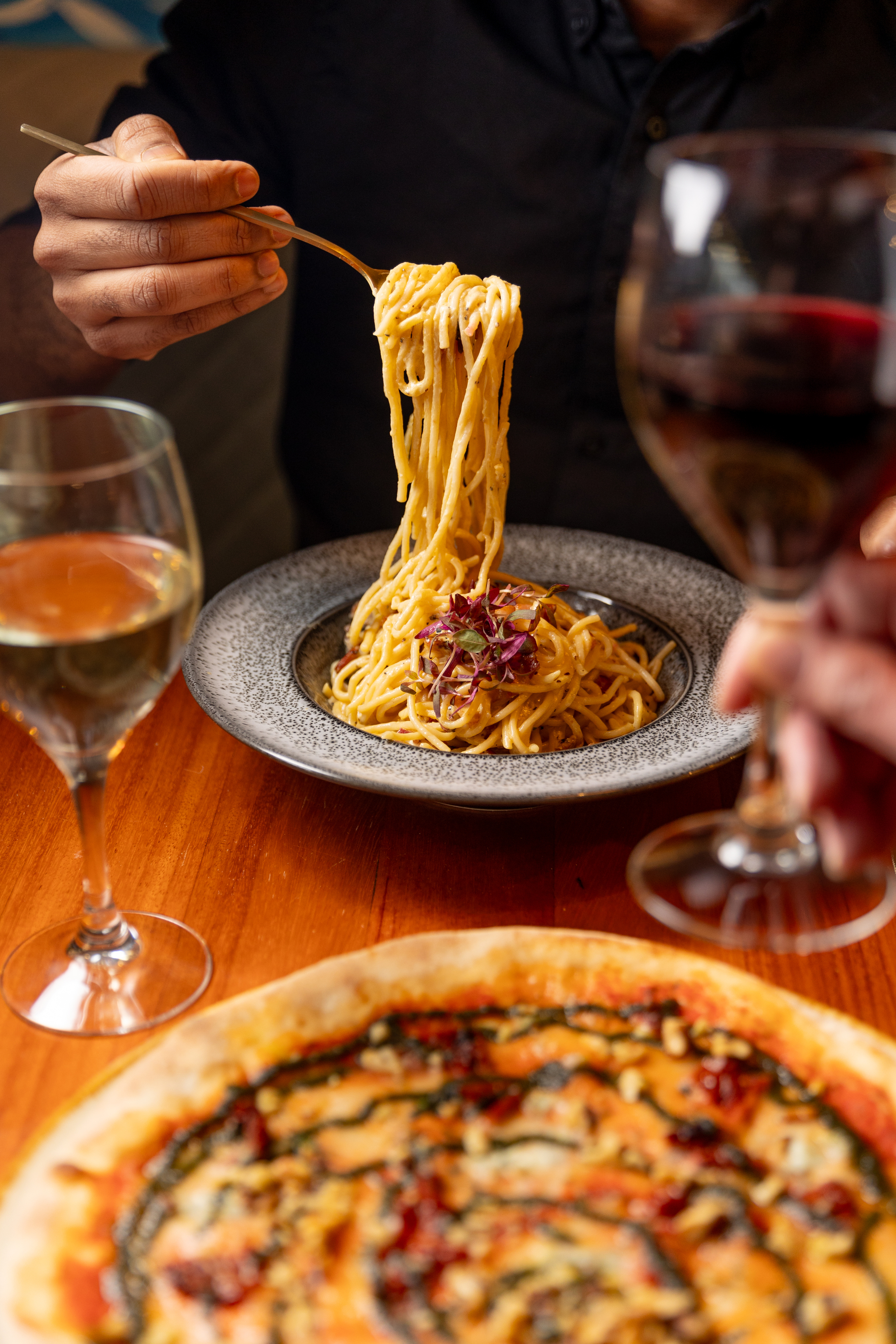 Hand with fork of spaghetti and pizza in foreground