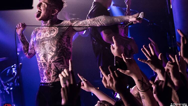 Singer covered in tattoos standing with his tongue out