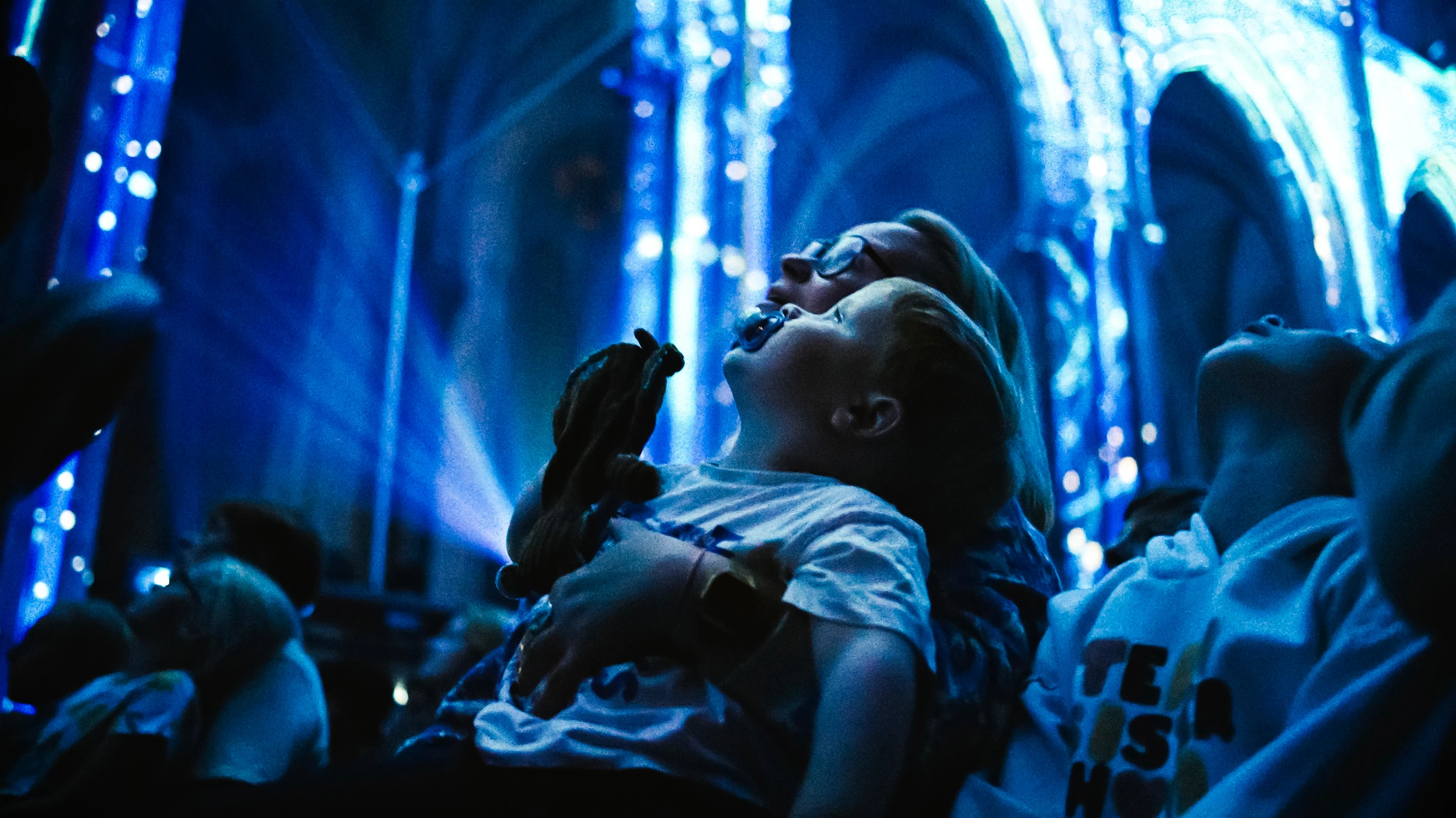 Woman holding baby and looking up to light show on building ceiling