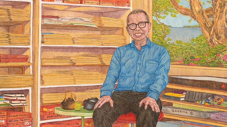 A smiling man sitting on a stool in front of an open window 