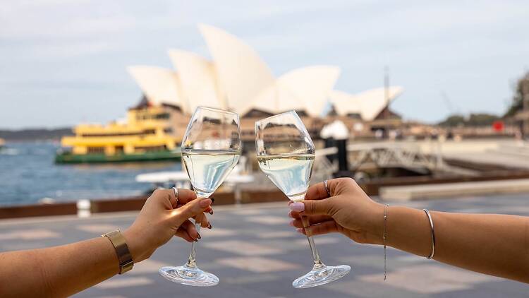 Two hands cheersing glasses of champagne in front of the Sydney Opera House