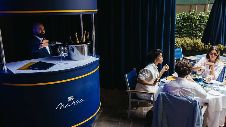 A patio with an outdoor bar and a person pouring Champagne