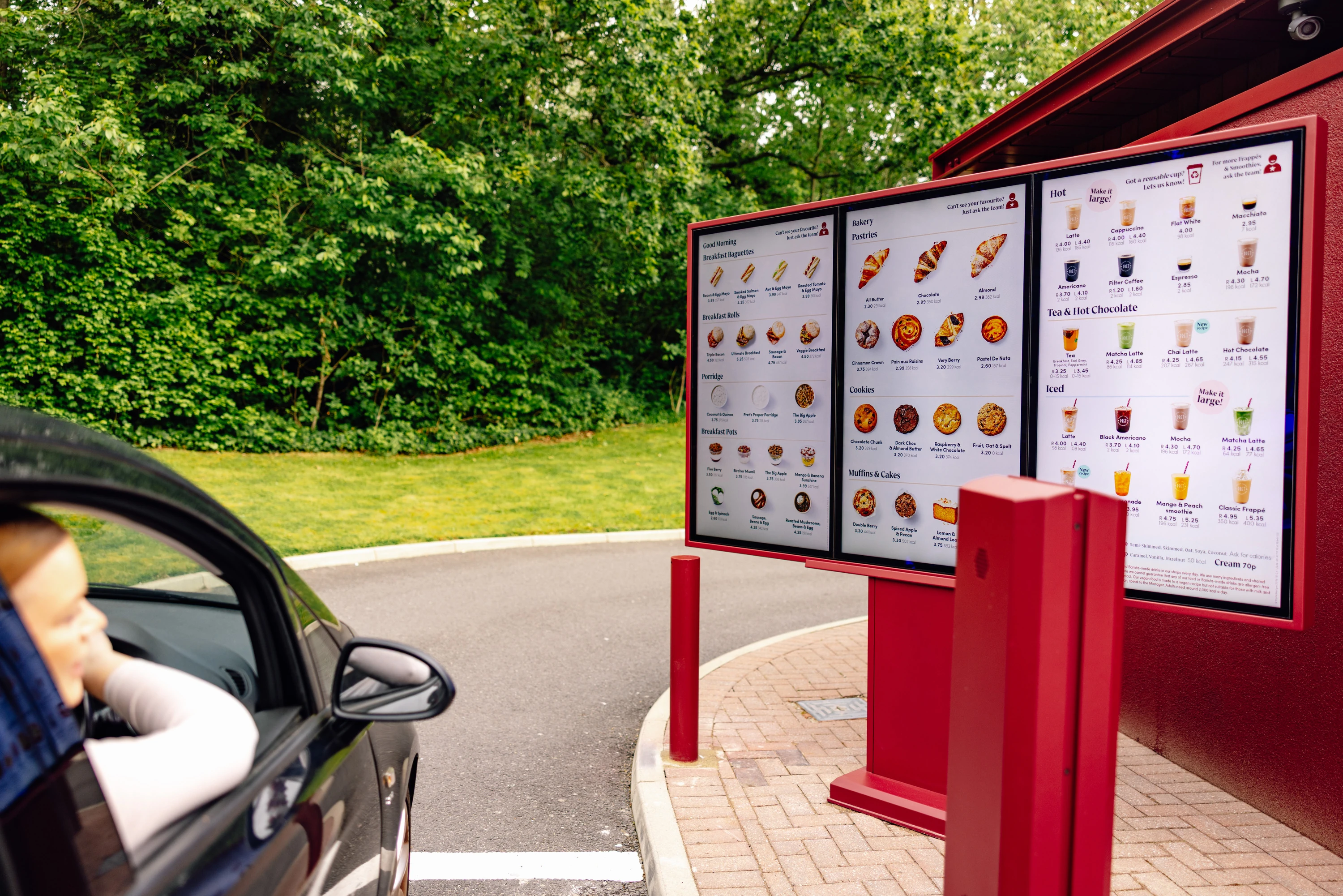Woman in car choosing from digital menu boards at Pret drive-thru