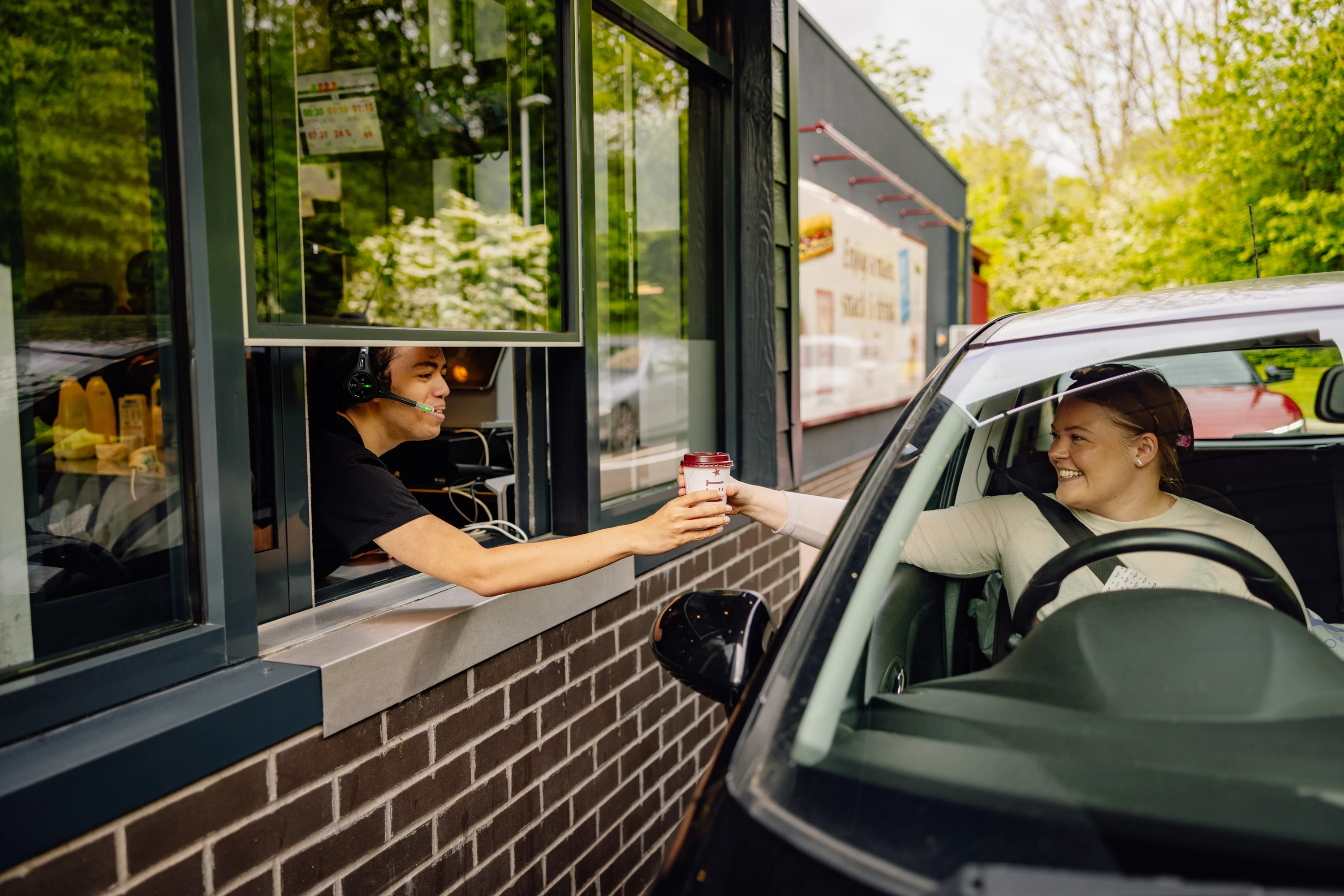 Server handing coffee to driver in car at Pret drive-thru