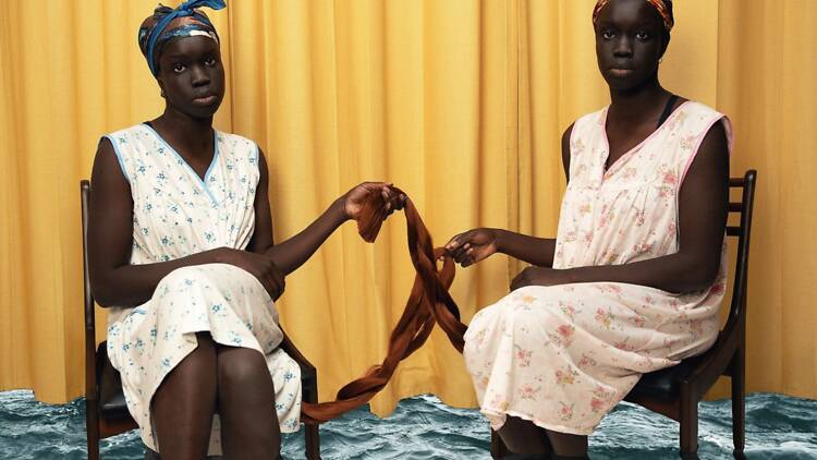 Atong Atem Two women sit on chairs and stare at camera.