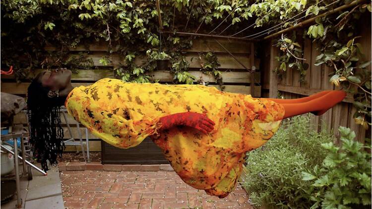 Atong Atem Woman in yellow dress levitates on her back.
